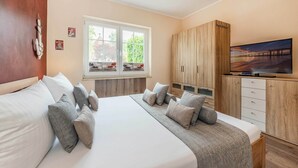 A bedroom with a large bed, a TV, wooden cabinets, and a window with a view. - Family-friendly vacation rental with a terrace and Wi-Fi—close to the beach in a quiet location (Koserow)