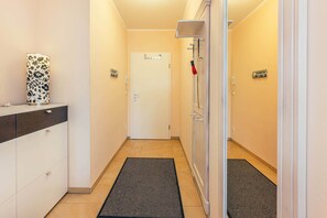Un couloir étroit avec une porte blanche, un tapis noir et un meuble blanc avec des tiroirs.