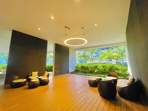 Ein moderner Lounge-Bereich mit Holzboden, runden Sitzgelegenheiten und Blick auf Grünflächen und Gebäude durch große Fenster.
