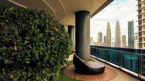 Ein Balkon mit einer grünen Hecke, einer runden schwarzen Sitzecke und Blick auf hohe Gebäude.