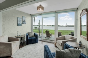A living room with a large sliding glass door to a patio, a sofa, a small table, and a decorative mirror. - Sea Palm View 5E (Fort Walton Beach)