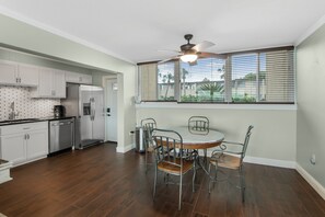 A kitchen with white cabinets, a stainless steel refrigerator, a dining table with metal chairs, and a ceiling fan. - Sea Palm View 5E (Fort Walton Beach)