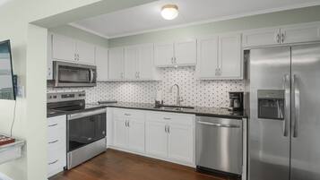 A modern kitchen with white cabinets, stainless steel appliances, and a tiled backsplash.