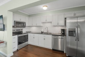 A modern kitchen with white cabinets, stainless steel appliances, and a tiled backsplash. - Sea Palm View 5E (Fort Walton Beach)