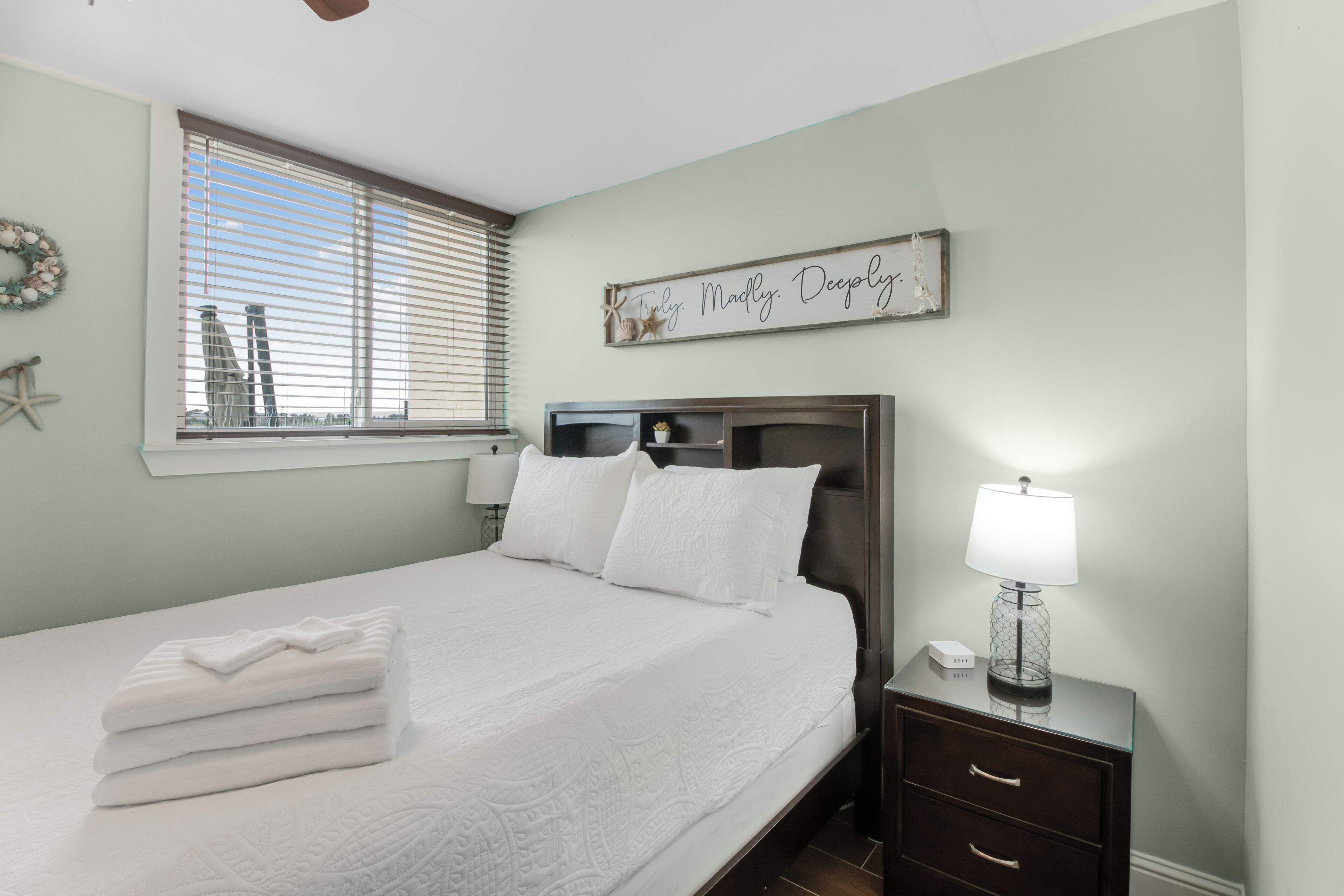 A neatly made bed with white linens, a bedside table with a lamp, and a wall decoration.