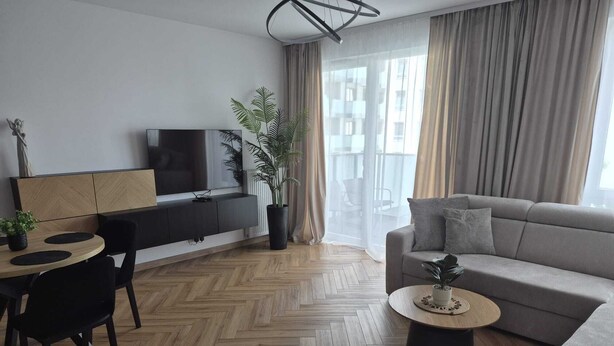 Una sala de estar moderna con un sofá, una mesa de comedor con sillas, un televisor sobre un mueble y una planta en maceta.