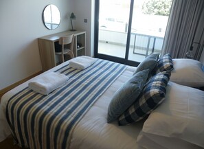 Una habitación de hotel con cama, escritorio, silla, ventana con vistas y espejo en la pared.