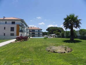 A residential building with a swimming pool, a well-maintained lawn, and a palm tree.
