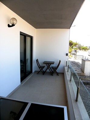 Un balcón con mesa y sillas, una puerta corrediza de vidrio y vista a la calle.