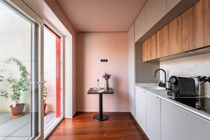 Eine moderne Küche mit einem Holzkasten, einer schwarzen Kaffeemaschine und einem kleinen Tisch mit einer Vase und einem Glas.