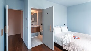 Ein Schlafzimmer mit einem Bett, einem Nachttisch und einem durch eine offene Tür einsehbaren Badezimmer.