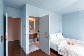 Ein Schlafzimmer mit einem Bett, einem Nachttisch und einem durch eine offene Tür einsehbaren Badezimmer.