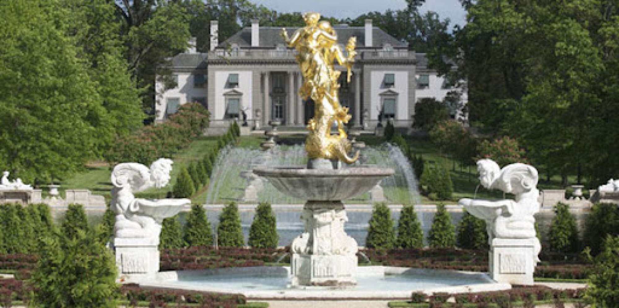A grand building with a fountain in the foreground, surrounded by manicured gardens and statues.