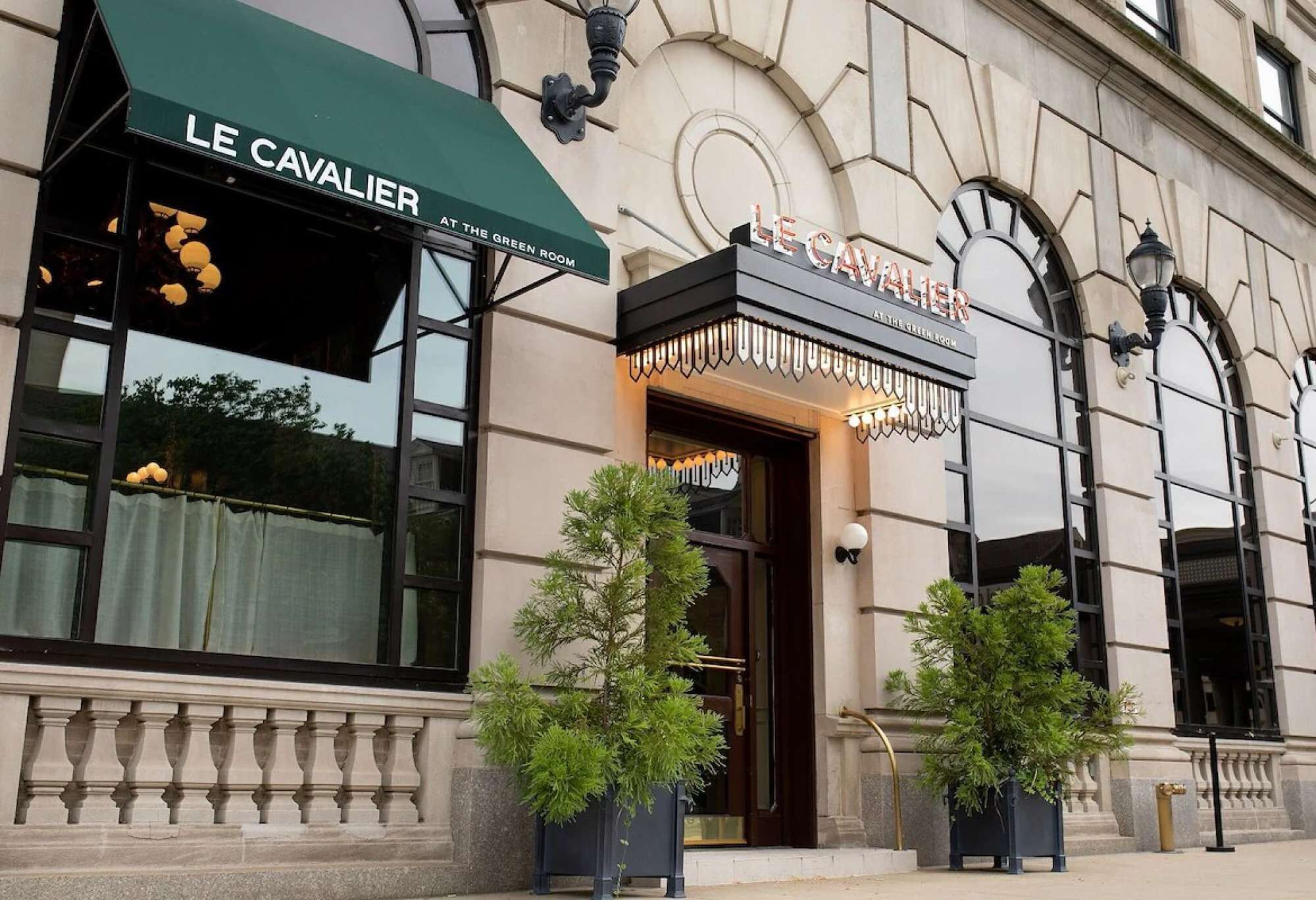 A building with a green awning labeled 'LE CAVALIER AT THE GREEN ROOM' and a sign above the entrance.