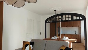A modern living room with a sofa, a dining table set, and a kitchen area visible through an archway.
