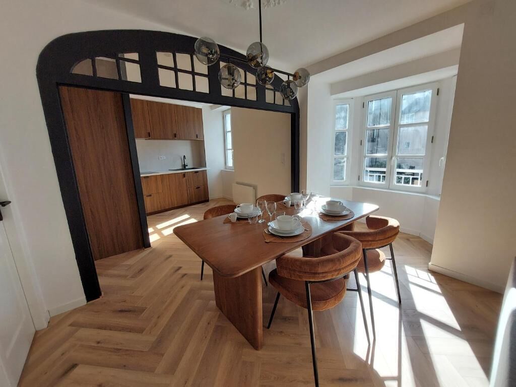 Un espace repas avec une table en bois, des chaises et une cuisine en arrière-plan.