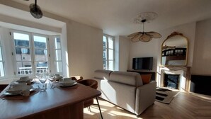 Un salón moderno con sofá, televisión y comedor con mesa dispuesta para una comida.