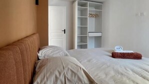 Un dormitorio con cama, almohadas, un armario y una mesita con una toalla.
