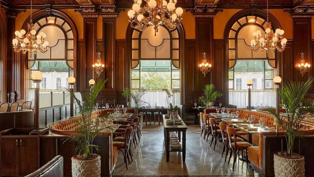 A spacious dining area with ornate chandeliers, wooden paneling, and large windows.