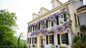 A historic building with a symmetrical facade, green shutters, and purple flowering vines.