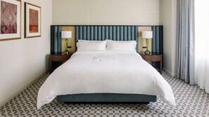 A hotel room with a large bed, two bedside tables with lamps, a headboard, and patterned carpet.