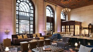 A spacious lounge with a large arched window, leather furniture, and a chandelier.