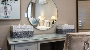Une salle de bain avec un miroir rond, un meuble-lavabo avec un plateau en verre et une œuvre d’art encadrée au mur.