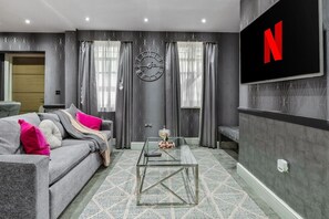 A modern living room with a grey sofa, a coffee table, a wall clock, and a TV displaying the Netflix logo. - Comfy & Spacious Marylebone Flat|Oxford Street (Greater London)