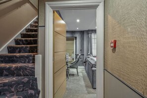 Un pasillo que conduce a un baño con ducha, lavabo e inodoro. Una escalera con alfombra estampada se encuentra a la izquierda.