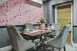 A dining area with a glass table, grey upholstered chairs, a pink flamingo wallpaper, and a wooden door. - Comfy & Spacious Marylebone Flat|Oxford Street (Greater London)