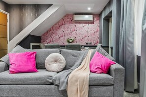 Un sofá gris con cojines rosa y beige, una pared con estampado de flamenco y una escalera.