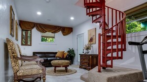 A living room with a brown leather sofa, a wooden chair, a red spiral staircase, a treadmill, and a marble floor.