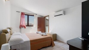 A hotel room with a bed, a desk, an air conditioning unit, a window with curtains, and a view of the outdoors.