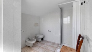 A bathroom with a shower, toilet, bidet, and a chair.