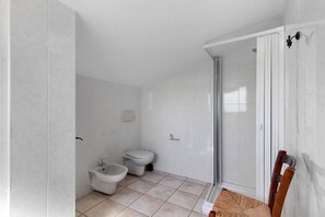 Une salle de bain équipée d’une douche, de toilettes, d’un bidet et d’une chaise.