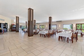 A spacious dining area with multiple tables and chairs, large pillars, and a view of the outdoors.