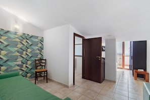 Una habitación con pared estampada, una puerta de madera, una cama verde y una silla.
