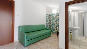 A room with a green sofa, a tiled floor, a patterned wall, and a bathroom with a sink and mirror.
