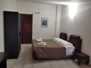 Ein Hotelzimmer mit Bett, Schreibtisch, Stuhl, Tür und einem gerahmten Bild an der Wand.