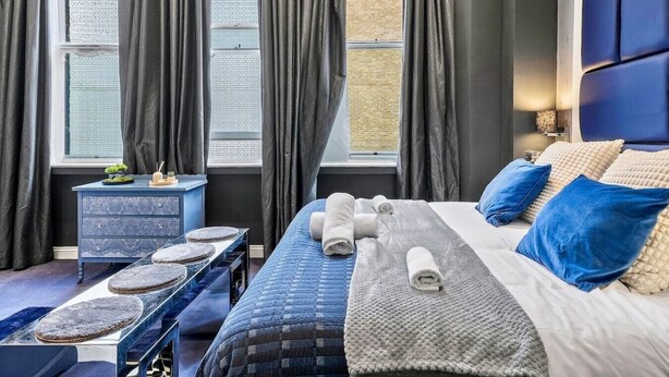 Une chambre d’hôtel avec un lit, une table de chevet, une fenêtre avec des rideaux et une vue sur un immeuble en briques.