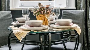 Une table à manger dressée pour deux personnes, avec un vase de fleurs, deux verres à vin et des assiettes.