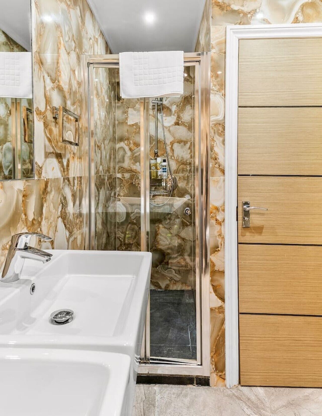A bathroom with a glass-enclosed shower, a white bathtub, and a wooden door.