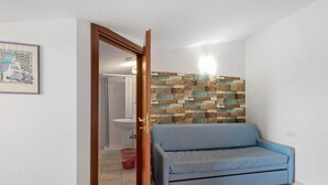 Een kamer met een blauwe bank, een houten wandpaneel, een witte wasbak en een deur naar een andere kamer.