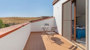 Een balkon met een tafel en stoelen, een schuifdeur die leidt naar een slaapkamer met een bed en handdoeken.