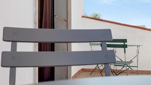 A white chair with a metal frame, positioned in front of a window with a view of a building and a clear sky. - Villa Ristòries Room 7 with Terrace, Wi-Fi, and Air Conditioning (Matera)