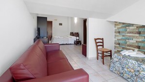 A hotel room with a red leather sofa, a bed with white linens, a wooden chair, and a wall with a rustic wood plank design. - Villa Ristòries Room 7 with Terrace, Wi-Fi, and Air Conditioning (Matera)