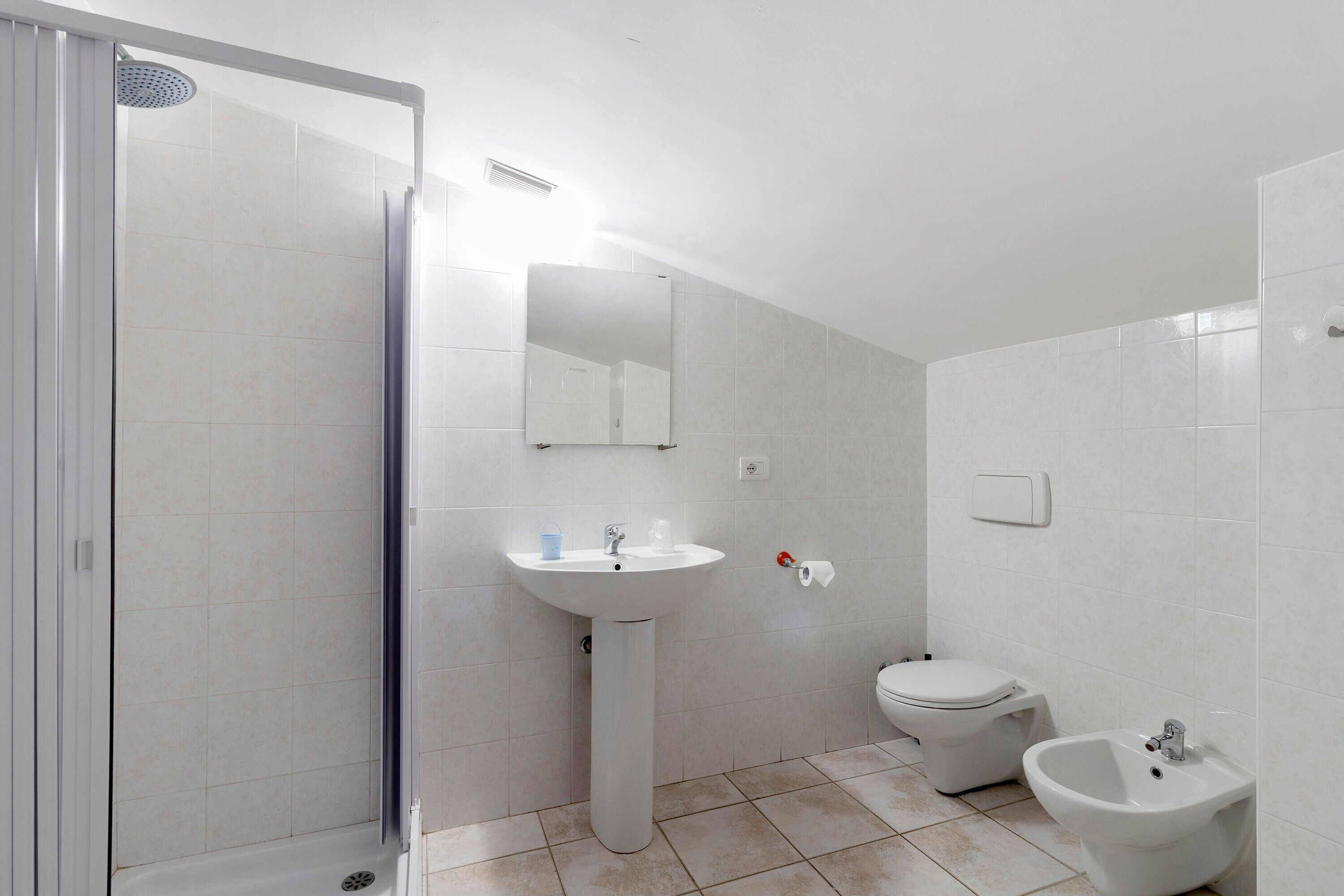 Un bagno completo di doccia, lavandino, wc, bidet e specchio.
