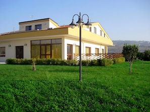 A modern two-story house with a large glass door, a small garden, and a view of the countryside.