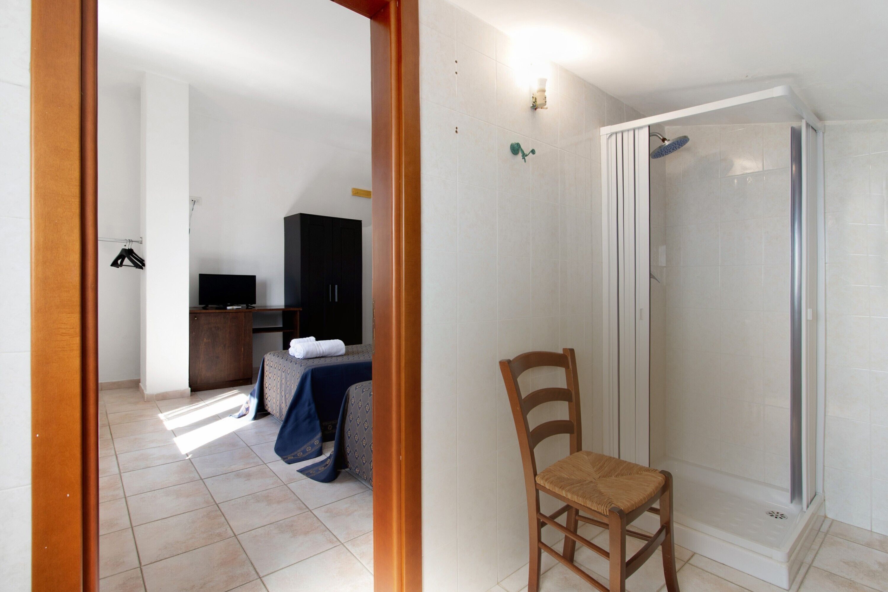 Una habitación con ducha, una silla, una cama con cubrecama azul y un televisor.