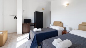 Een hotelkamer met twee bedden, een kledingkast, een bureau met een televisie en een kleine tafel met een lamp.